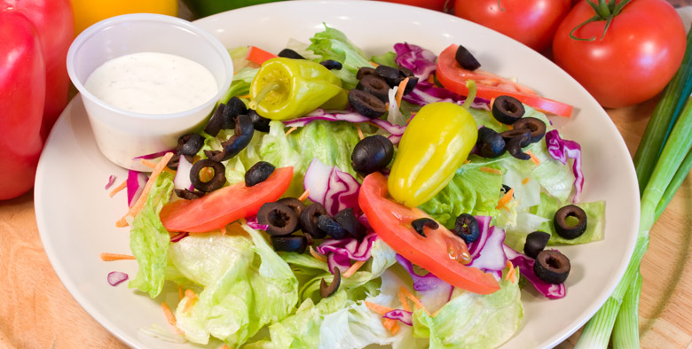 A salad with Peppers, Black Olives, carrot strips and a side of ranch dressing.