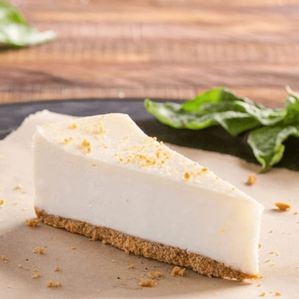 A slice of Ameci Pizza & Pasta's creamy cheesecake with a graham cracker crust and green garnish.