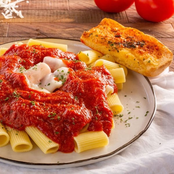Rigatoni pasta with red sauce, melted mozzarella, and a side of garlic bread on a white plate.