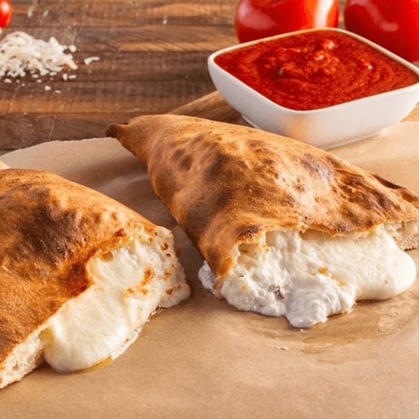 Two Ameci calzones, one cut open with melted cheese spilling out, alongside a bowl of marinara.